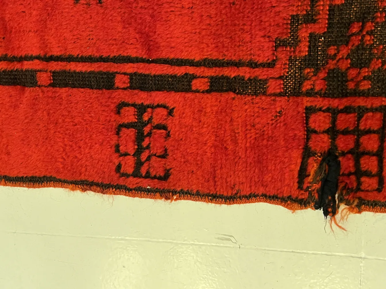 Details of an antique red carpet with black patterns.