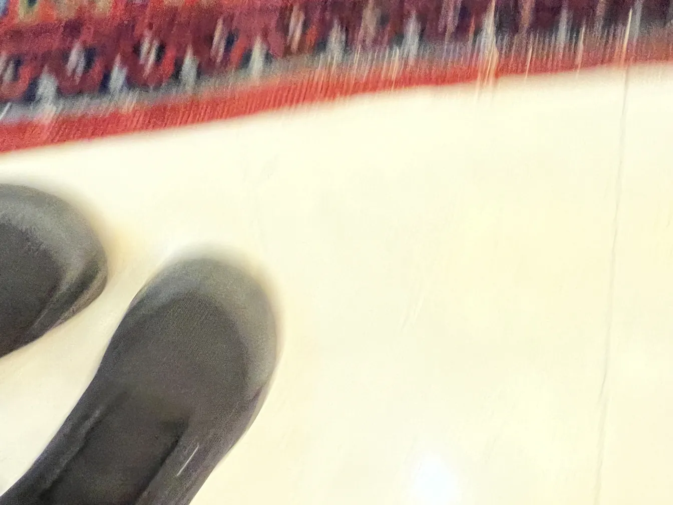 Tappeto antico multicolore su sfondo chiaro con scarpe nere.