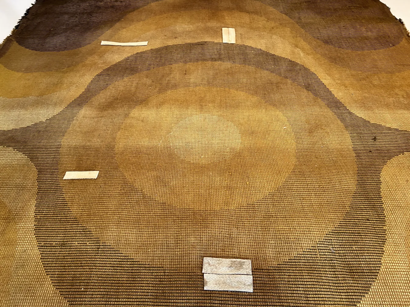 Tappeto antico con motivi geometrici in toni marroni e beige, in un ambiente accogliente.