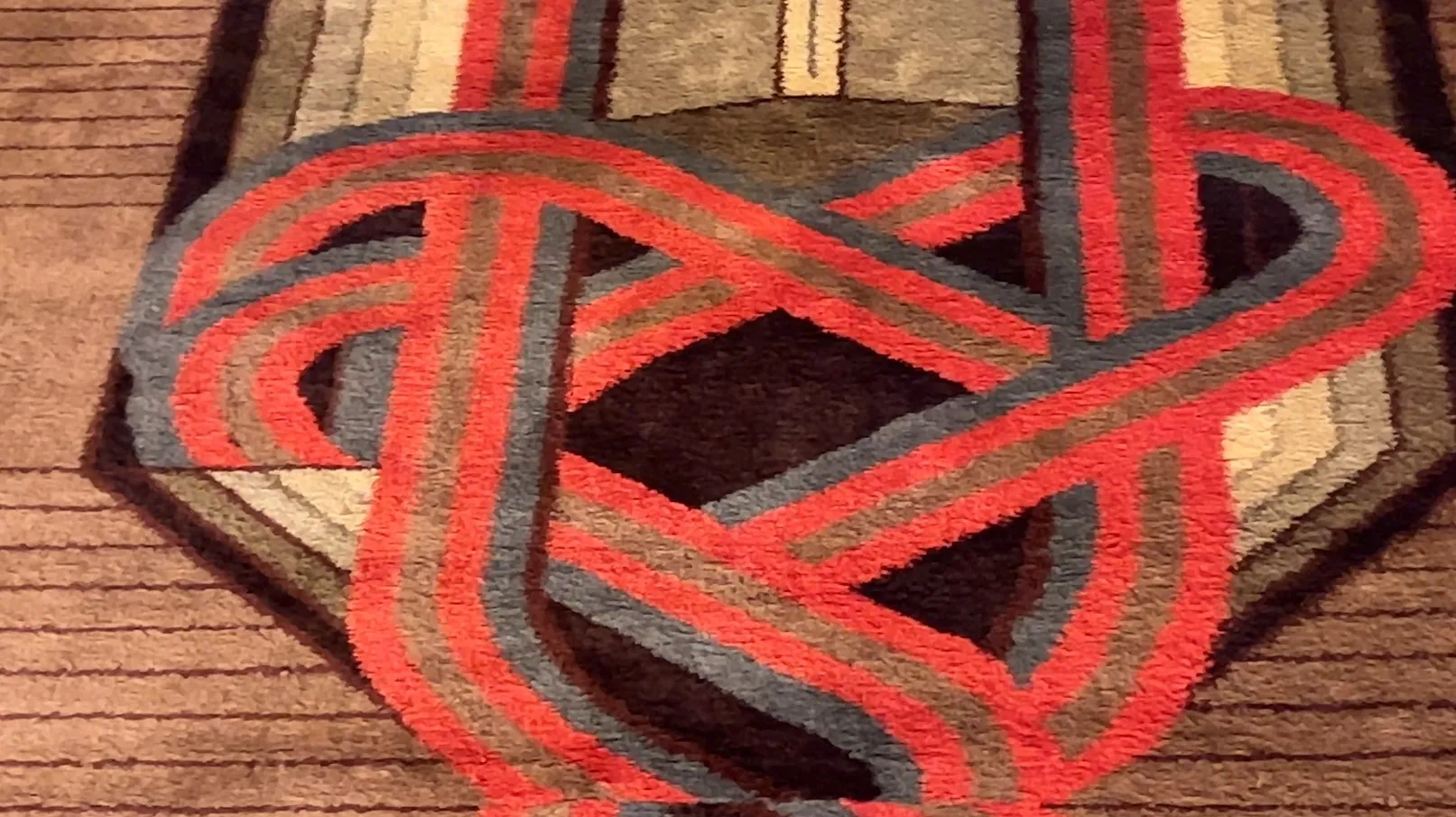 alfombra antigua con patrones en tonos rojo y gris sobre un fondo marrón