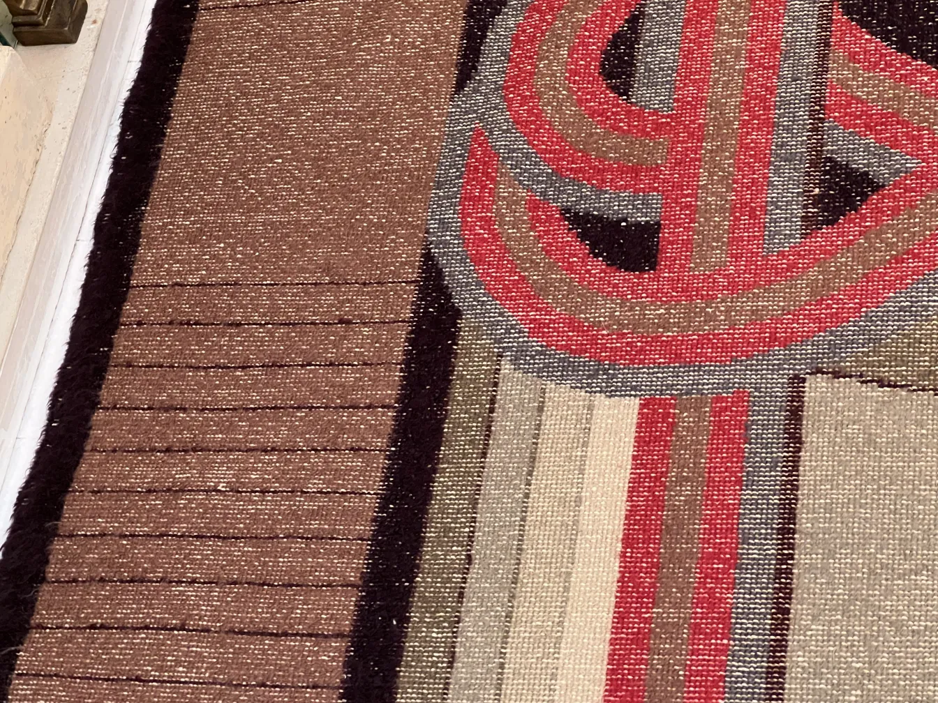 Tappeto antico con design colorato in tonalità marroni e rosse.