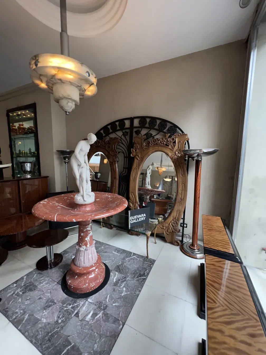 Antigua fuente de mármol rosa con figura en el centro y espejo decorativo.