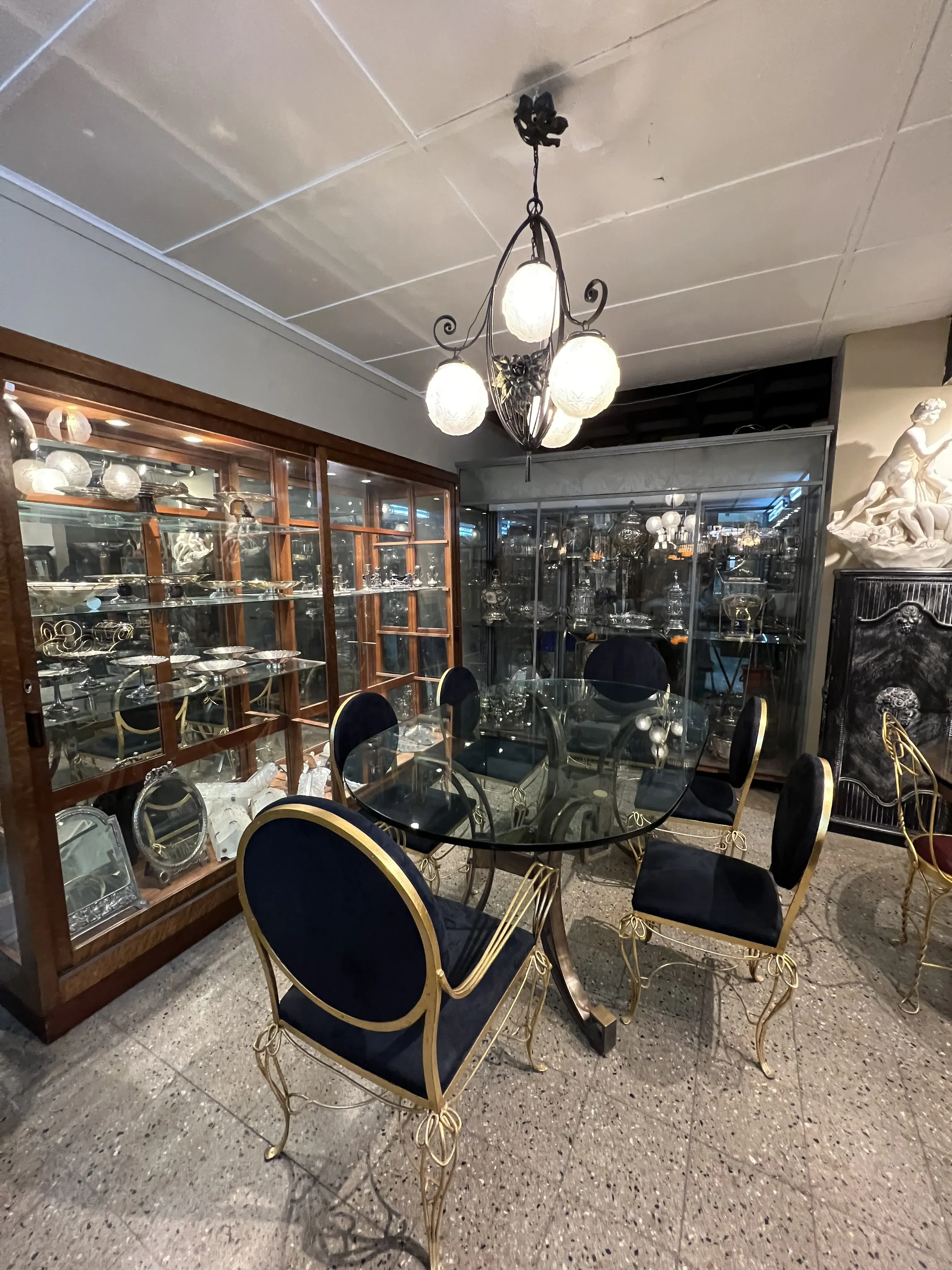 Mesa de jantar antiga Art Deco com cadeiras azuis em um ambiente elegante, cercada por vitrines.