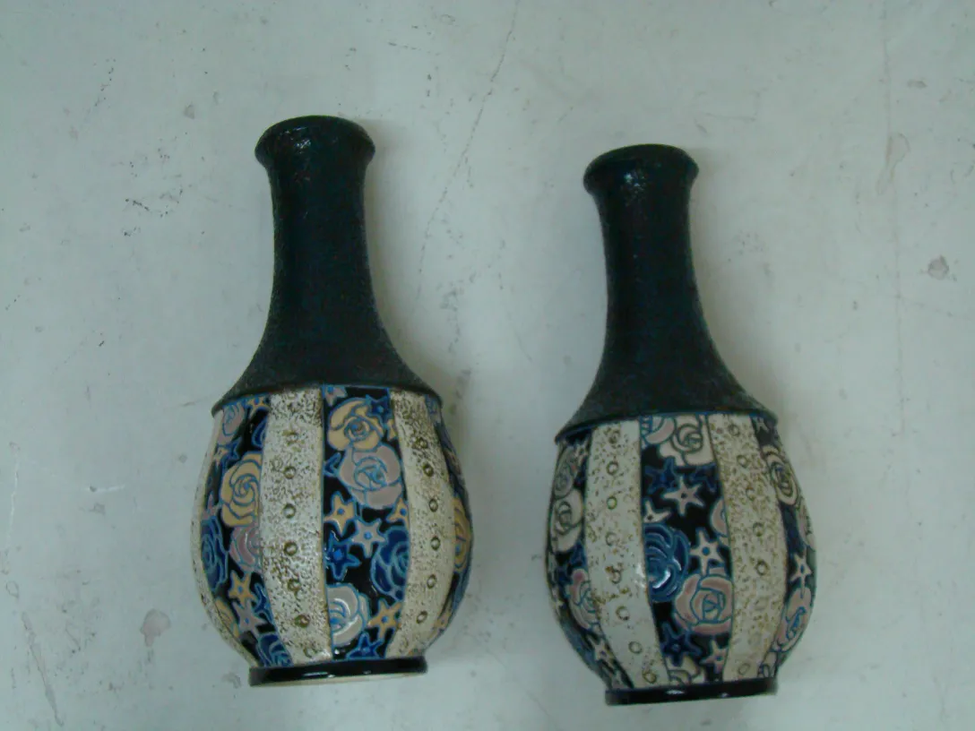 dos jarrones antiguos de cerámica con decoración floral y colorida. En el fondo, un ambiente neutro.