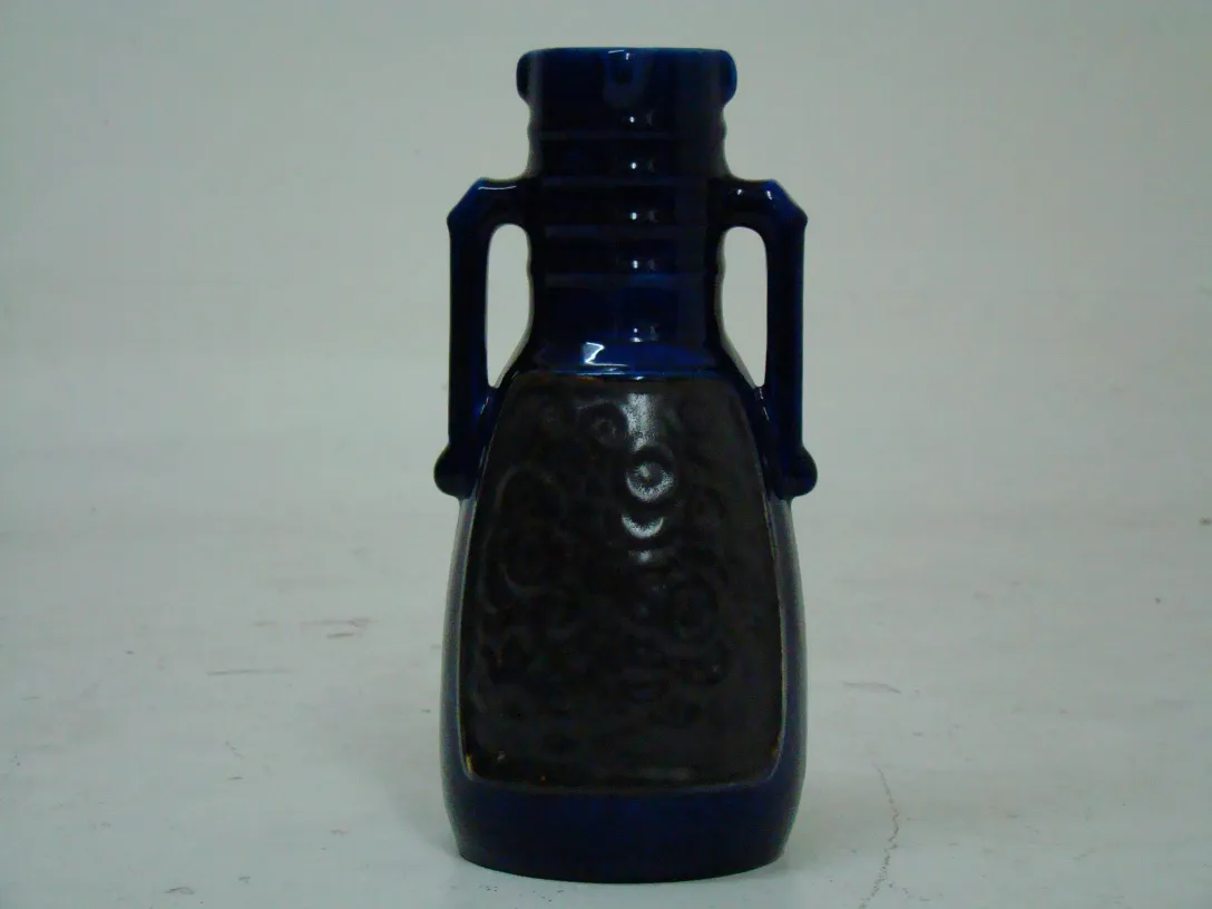 Antica vase in ceramica blu con manici decorativi su sfondo chiaro.