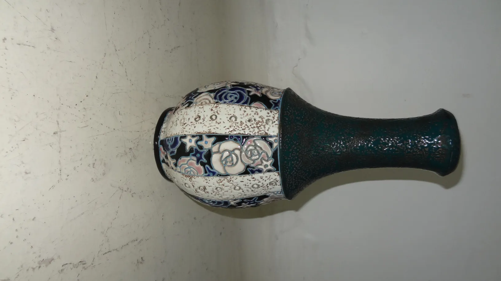 Vaso antigo de cerâmica decorado com designs florais em cores escuras e claras.