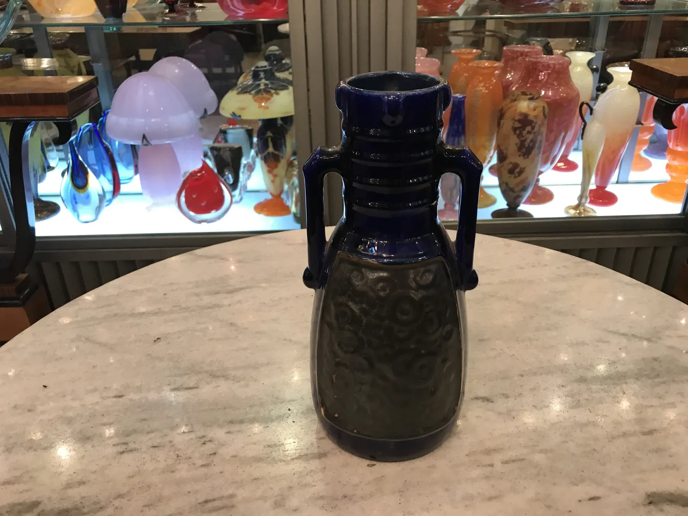 Vaso antico in ceramica blu e nera con design a spirale, circondato da antiquariato colorato.