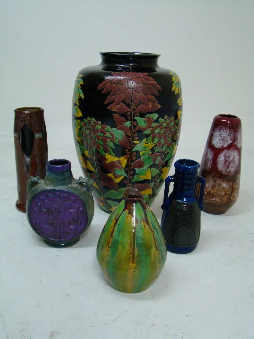 Plusieurs vases en céramique anciens aux couleurs vives et motifs uniques sur une table blanche.