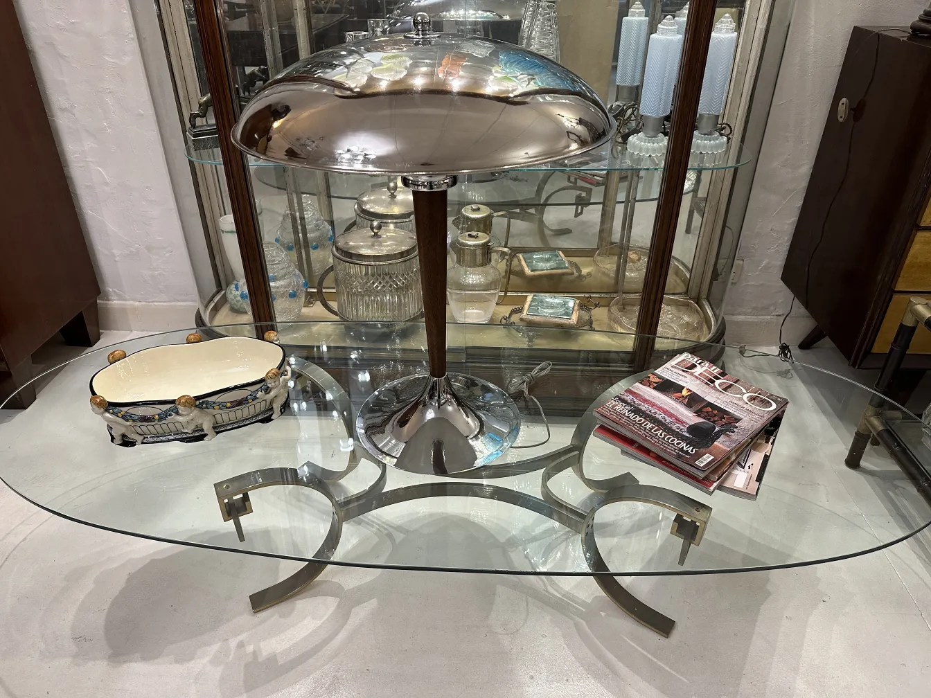 Plateau de céramique ancien avec des détails colorés, exposé sur une table en verre avec lampe.