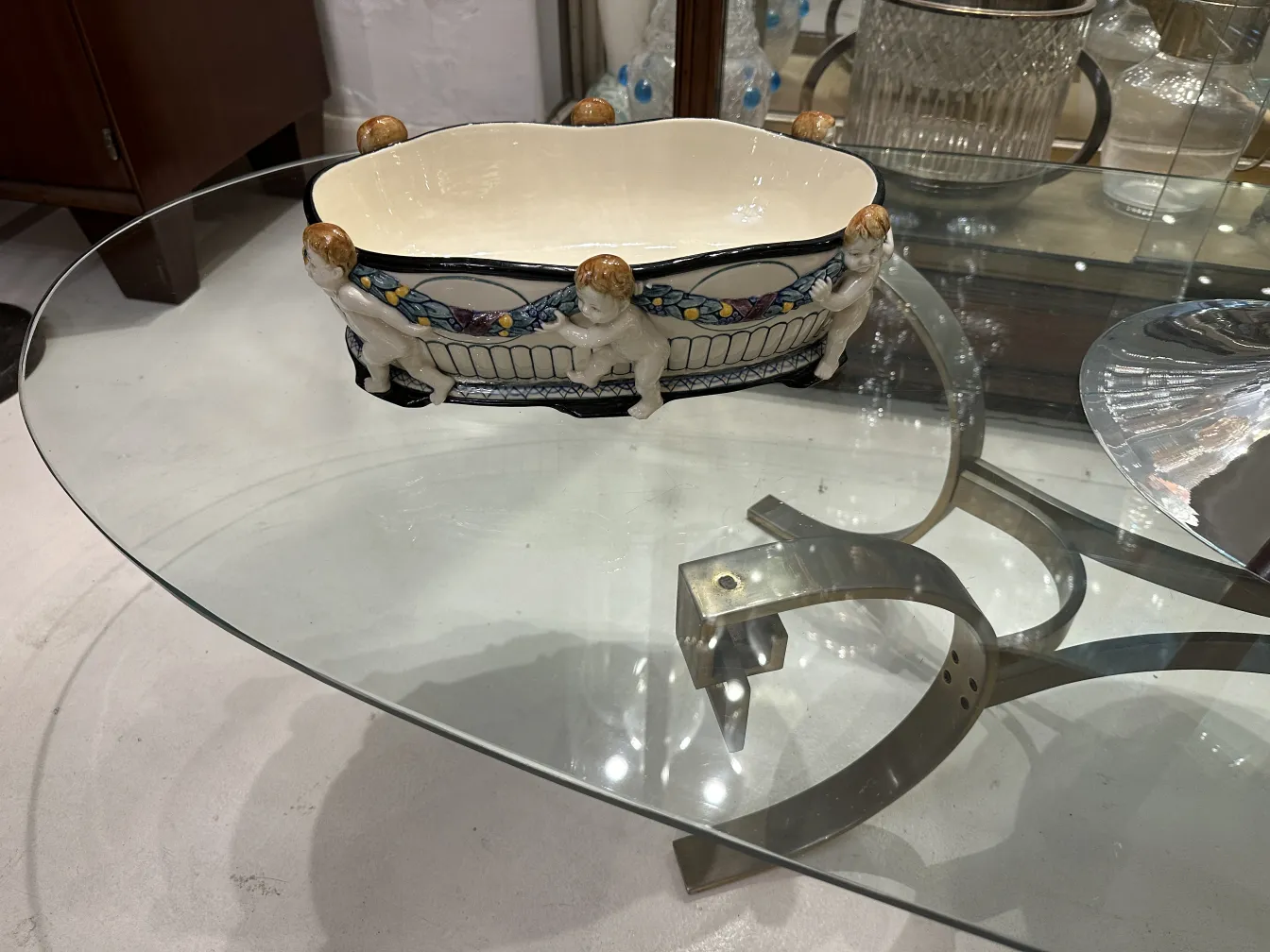 Antique ceramic decorated with figures and bright colors displayed on a glass table.