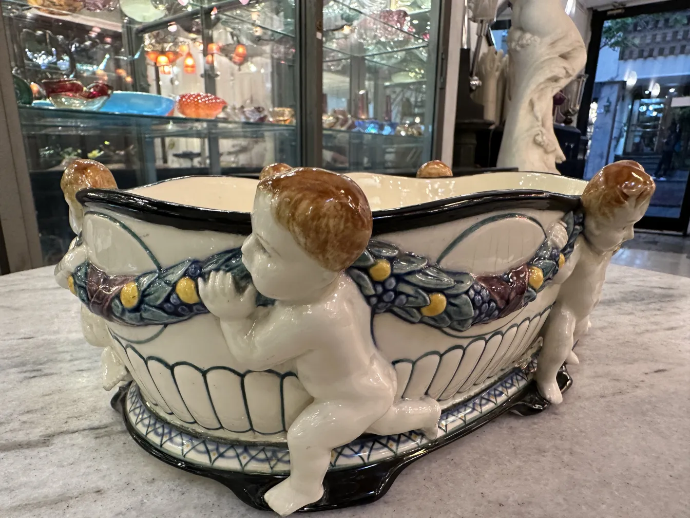 Ceramica antica decorata con figure di bambini scolpiti, sfondo luminoso.