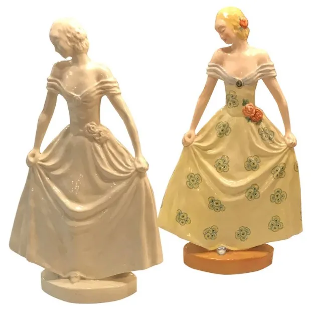 Figures en céramique anciennes de femmes, l'une en robe blanche et l'autre en jaune avec des fleurs, sur des bases décoratives.