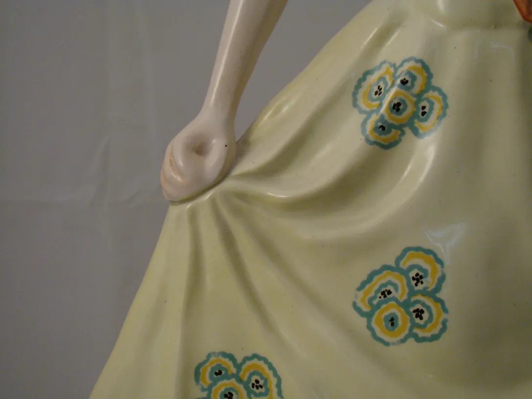 Figura feminina de cerâmica antiga com vestido amarelo decorado.