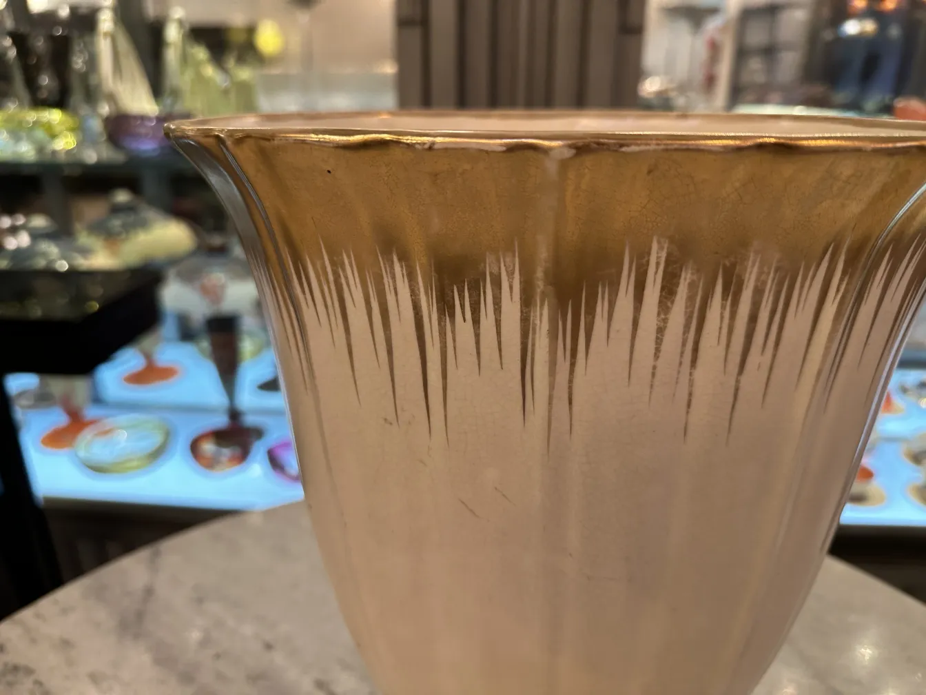 Vase en céramique ancienne avec des décorations dorées et un design élégant, fond flou avec divers objets.