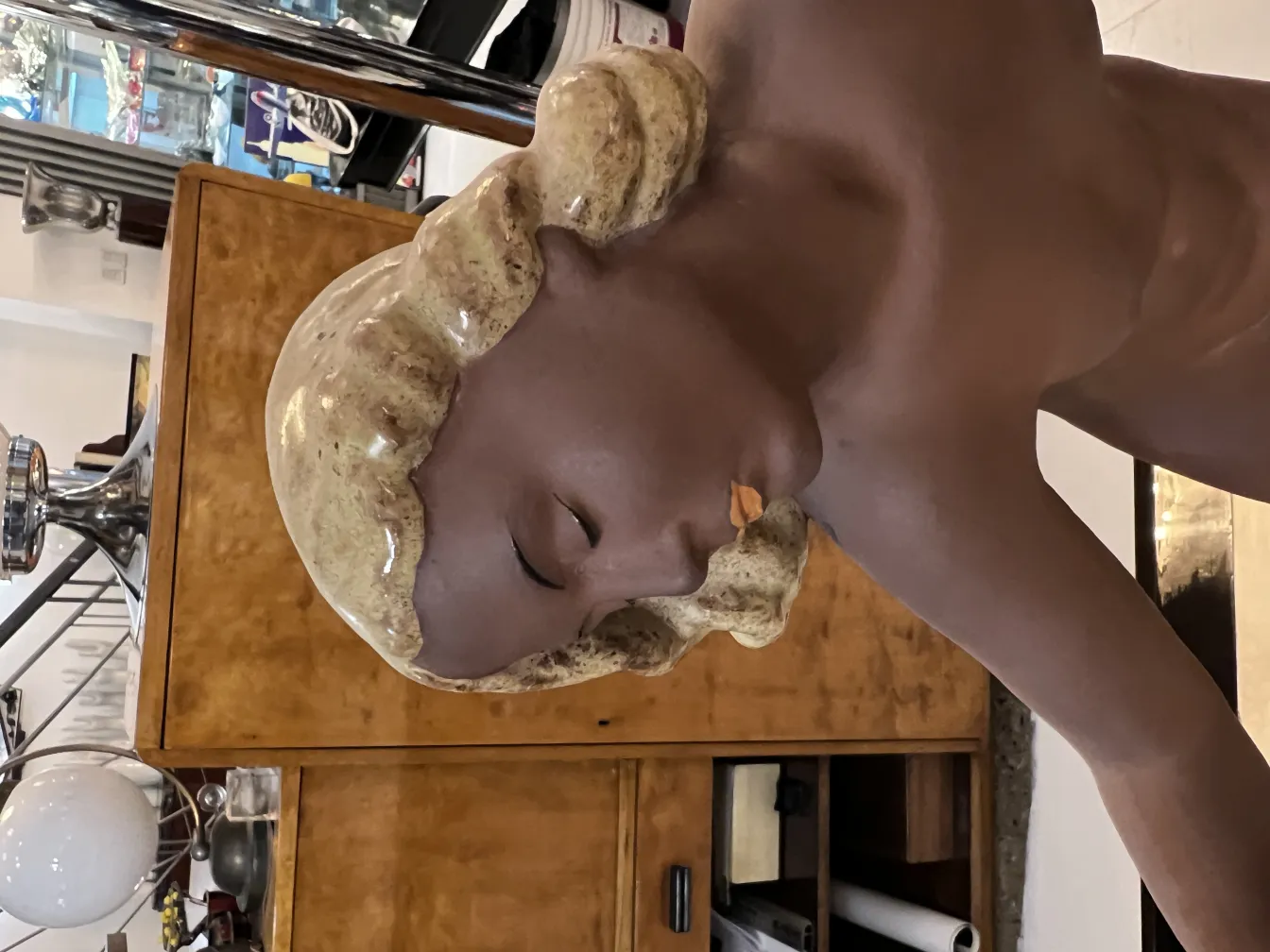 Ritratto in ceramica antica con dettagli decorativi e espressione serena, sfondo con mobili semplici.