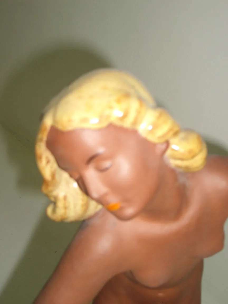 Antica scultura di ceramica di donna con capelli biondi e volto sereno, sfondo chiaro.
