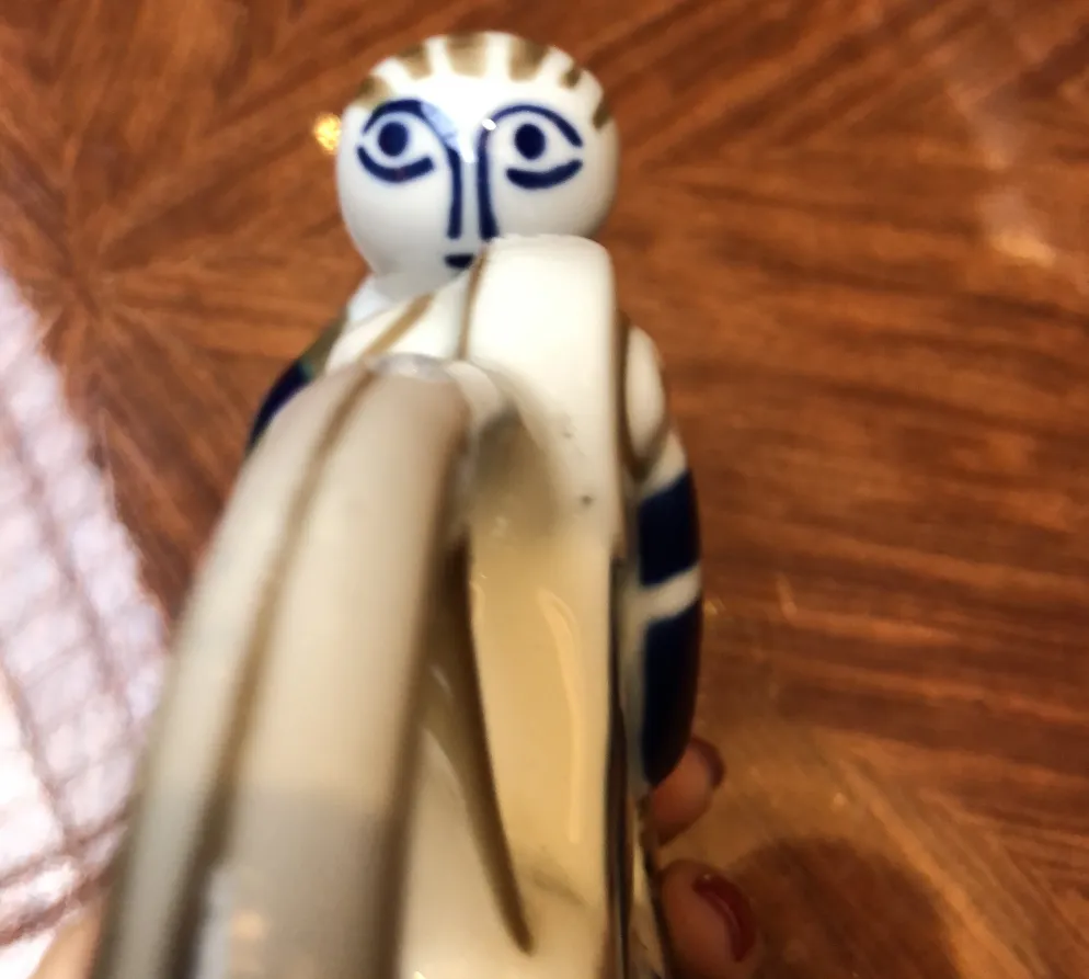 figurina antica in ceramica con dettagli blu e faccia espressiva, sfondo di tavolo in legno lucido