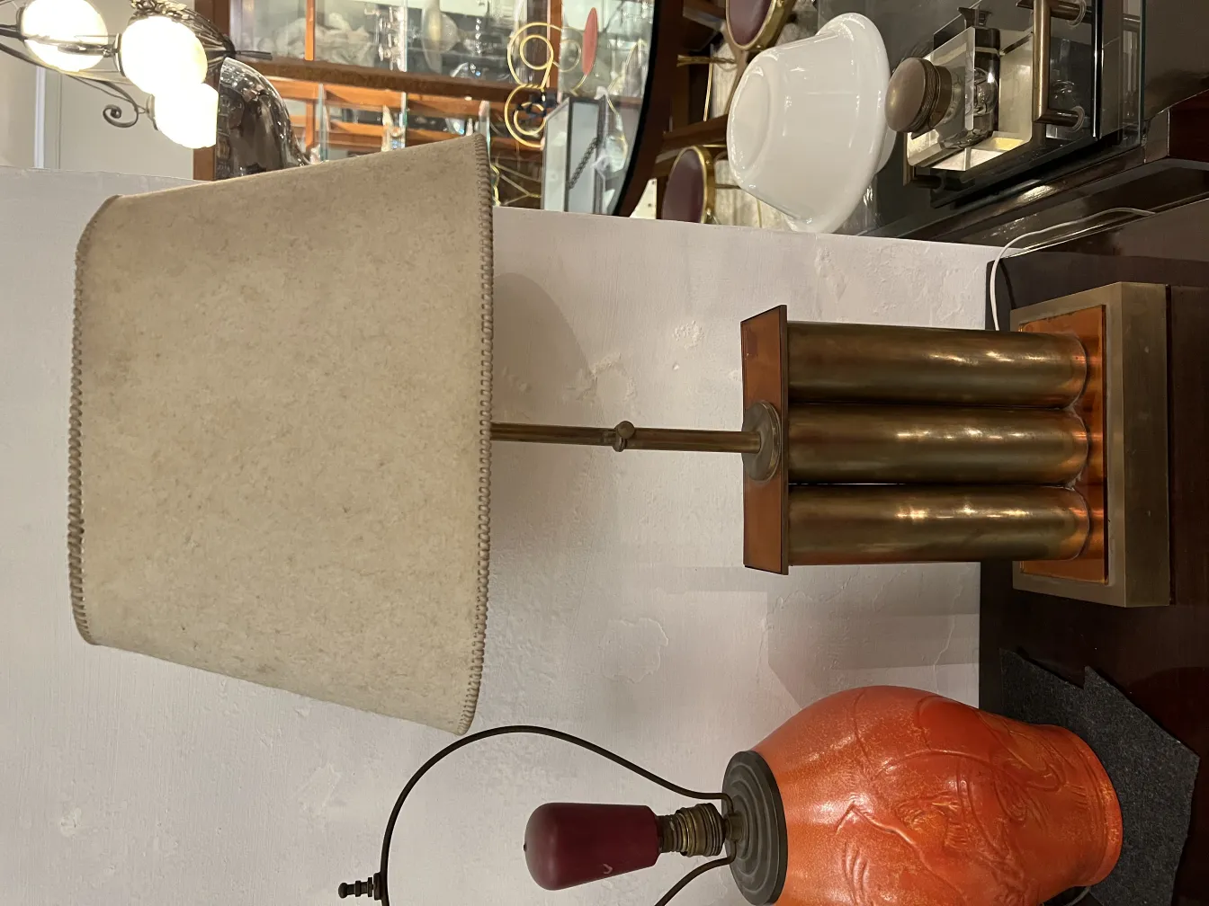 Antigua lámpara de mesa con base de diseño y pantalla beige, rodeada de un ambiente clásico.