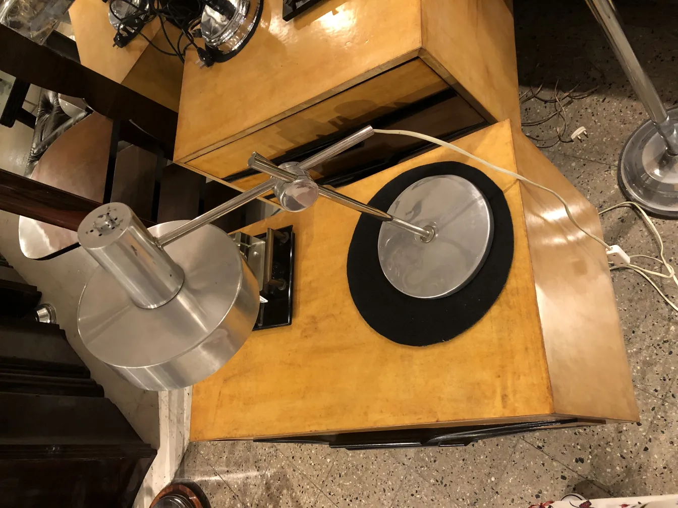 Antique table lamp with circular base and modern design. Background features light wooden table.