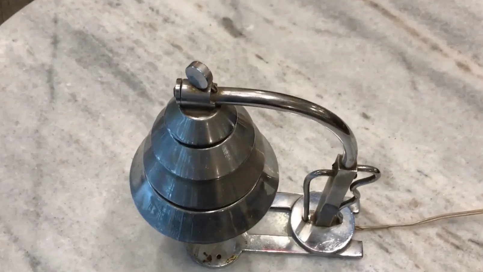 Antike Tischlampe mit markantem und elegantem Design, glänzende metallische Töne, auf einer hellen Oberfläche.