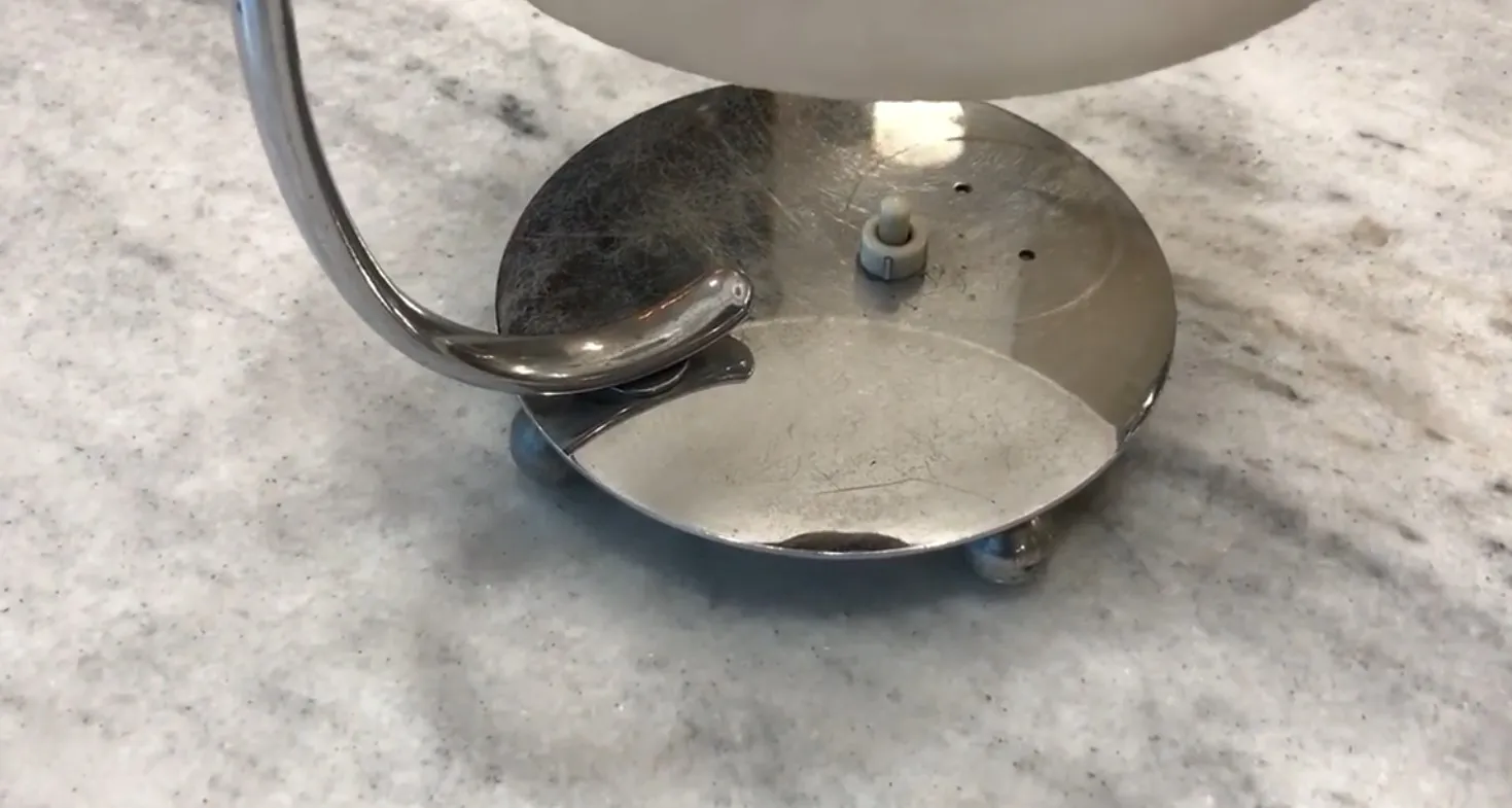 Antike Tischlampe mit glänzender Basis und subtilen Details in einer neutralen Umgebung.