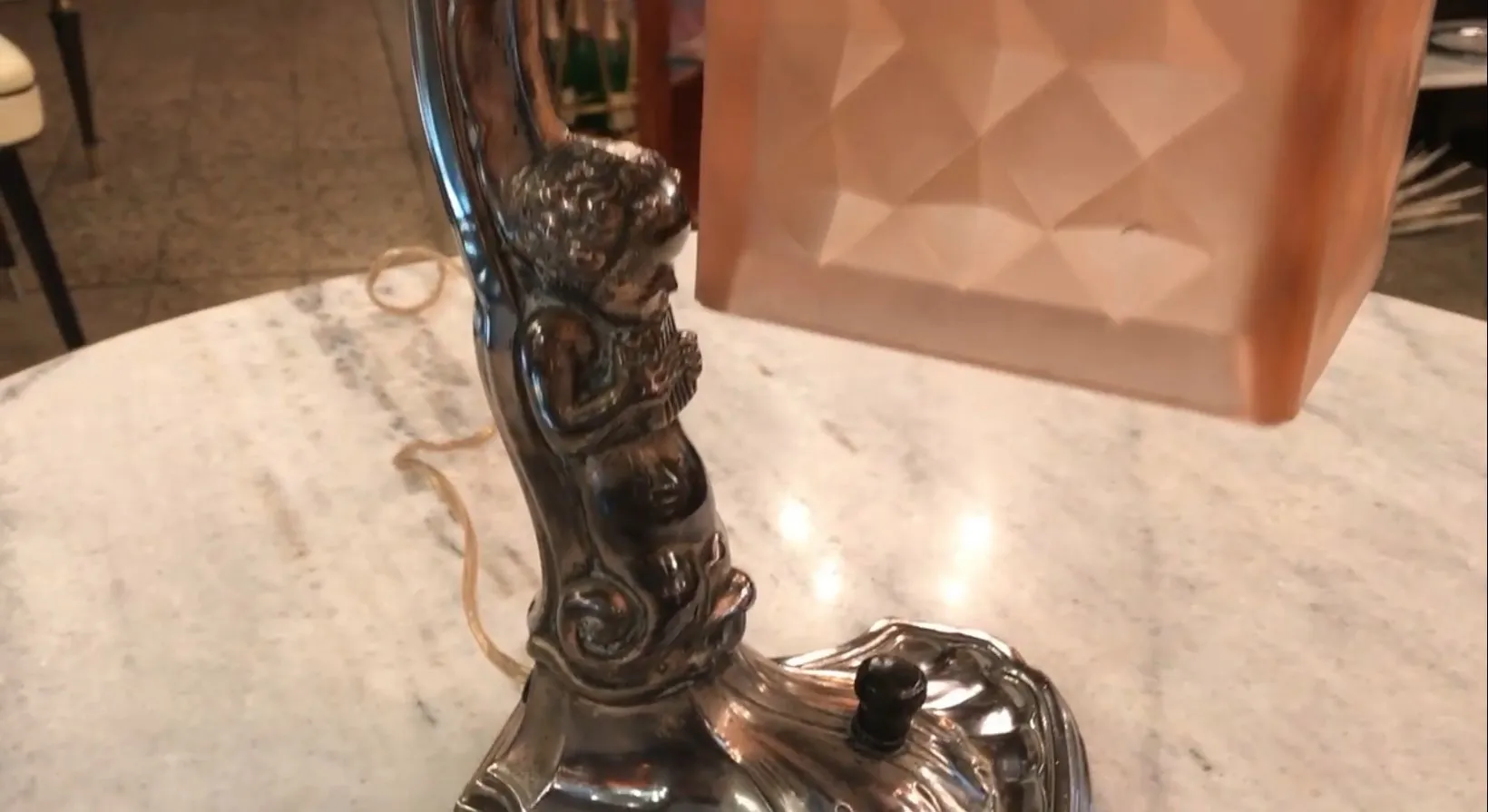 Lámpara de mesa antigua con base decorada y escultura. Entorno cálido.