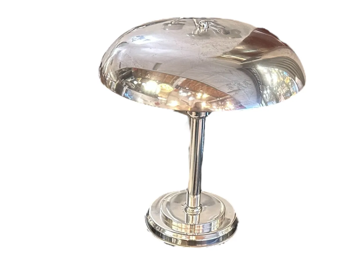 Une lampe de bureau ancienne avec une base brillante et une forme arrondie, éclairant doucement un cadre confortable.