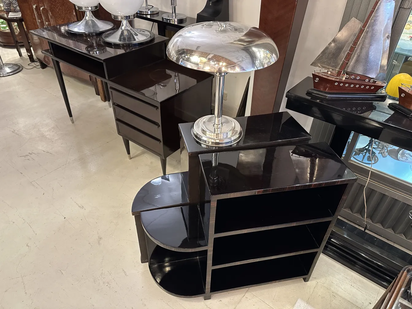 Lampada da tavolo antica con base in metallo lucido, su un mobile scuro.