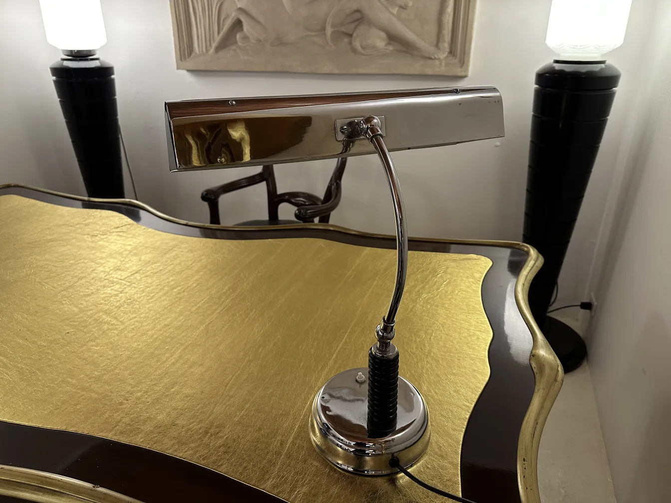 Lámpara de mesa antigua con base brillante en un escritorio dorado, rodeada de otros elementos de decoración.