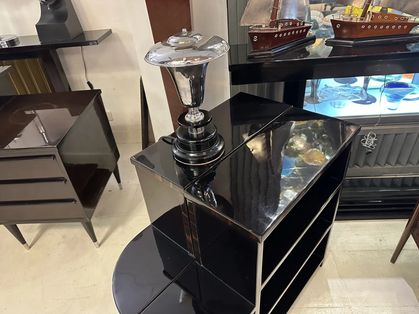 Lámpara de mesa antigua con base negra y detalles brillantes, en un entorno de antigüedades.