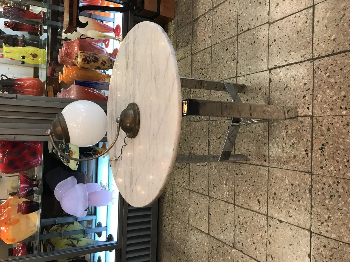 Lampada da tavolo antica con base in metallo e paralume bianco, circondata da oggetti decorativi colorati.