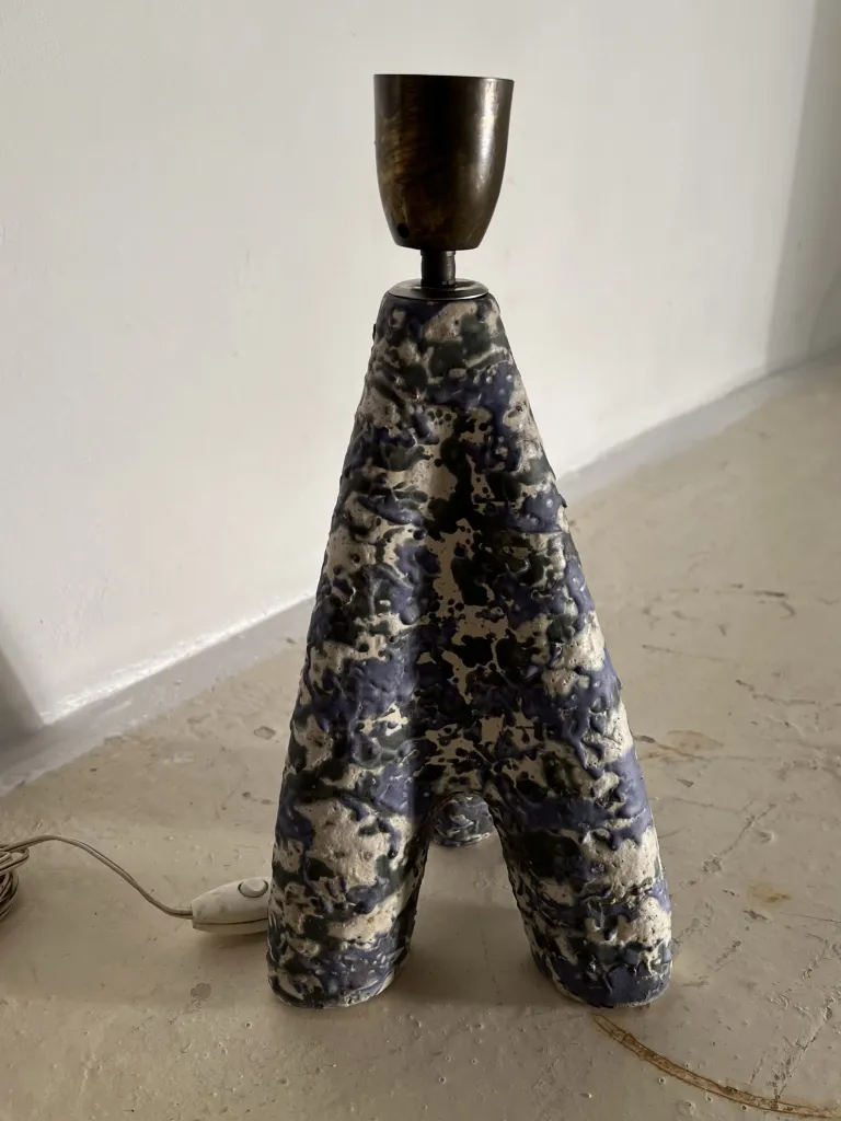 Lámpara de mesa antigua con un diseño abstracto y base en forma de A sobre una superficie clara.