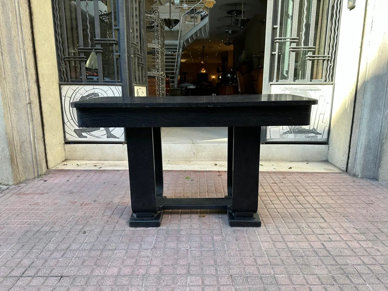 Antiga consola decorativa preta em frente a portas de vidro