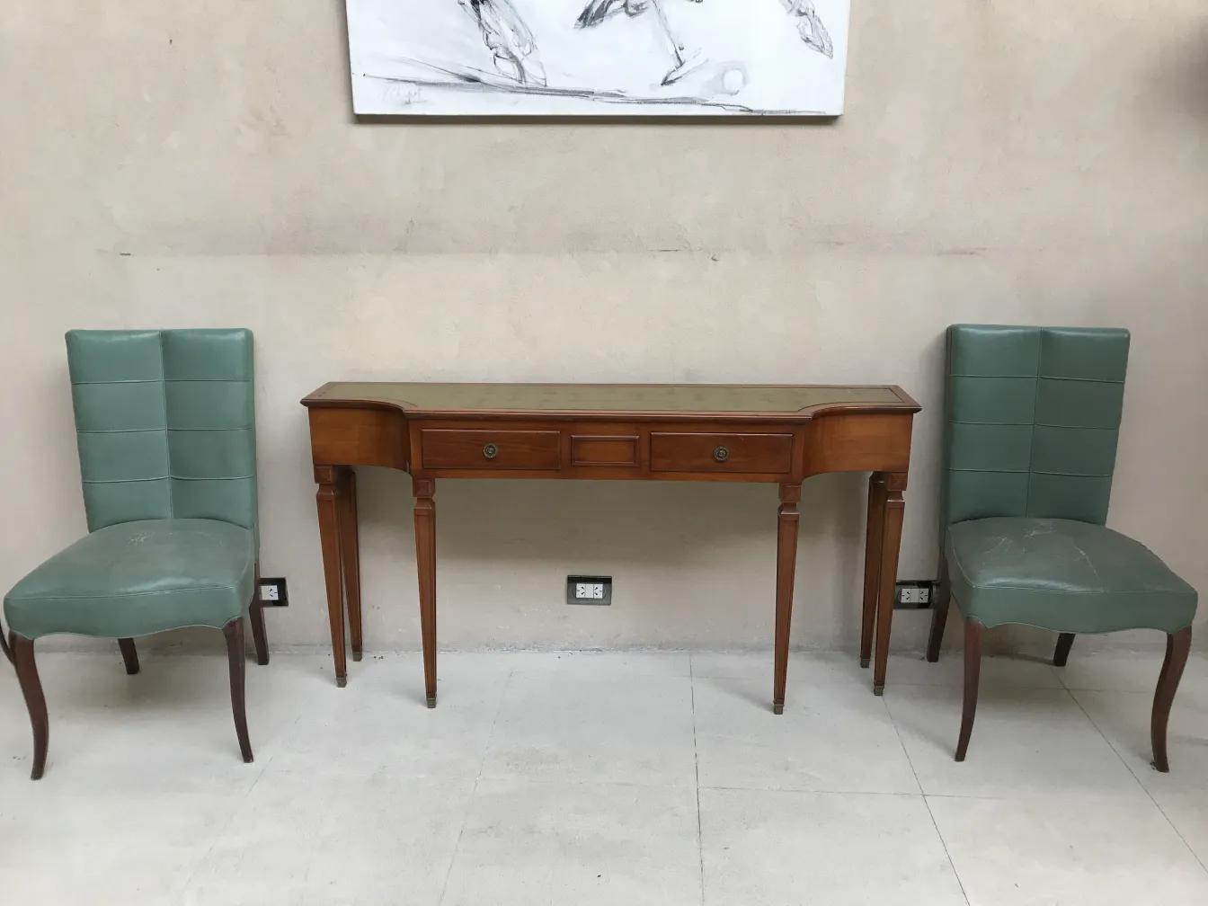 Consola antigua con dos cajones y diseño clásico, flanqueada por sillas modernas.