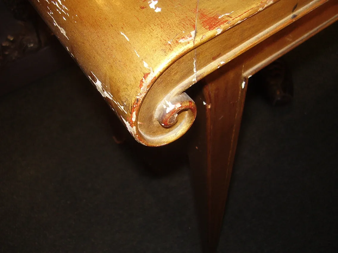 Close-up de uma antiga consola rateau-armand com detalhes dourados, mostrando desgaste