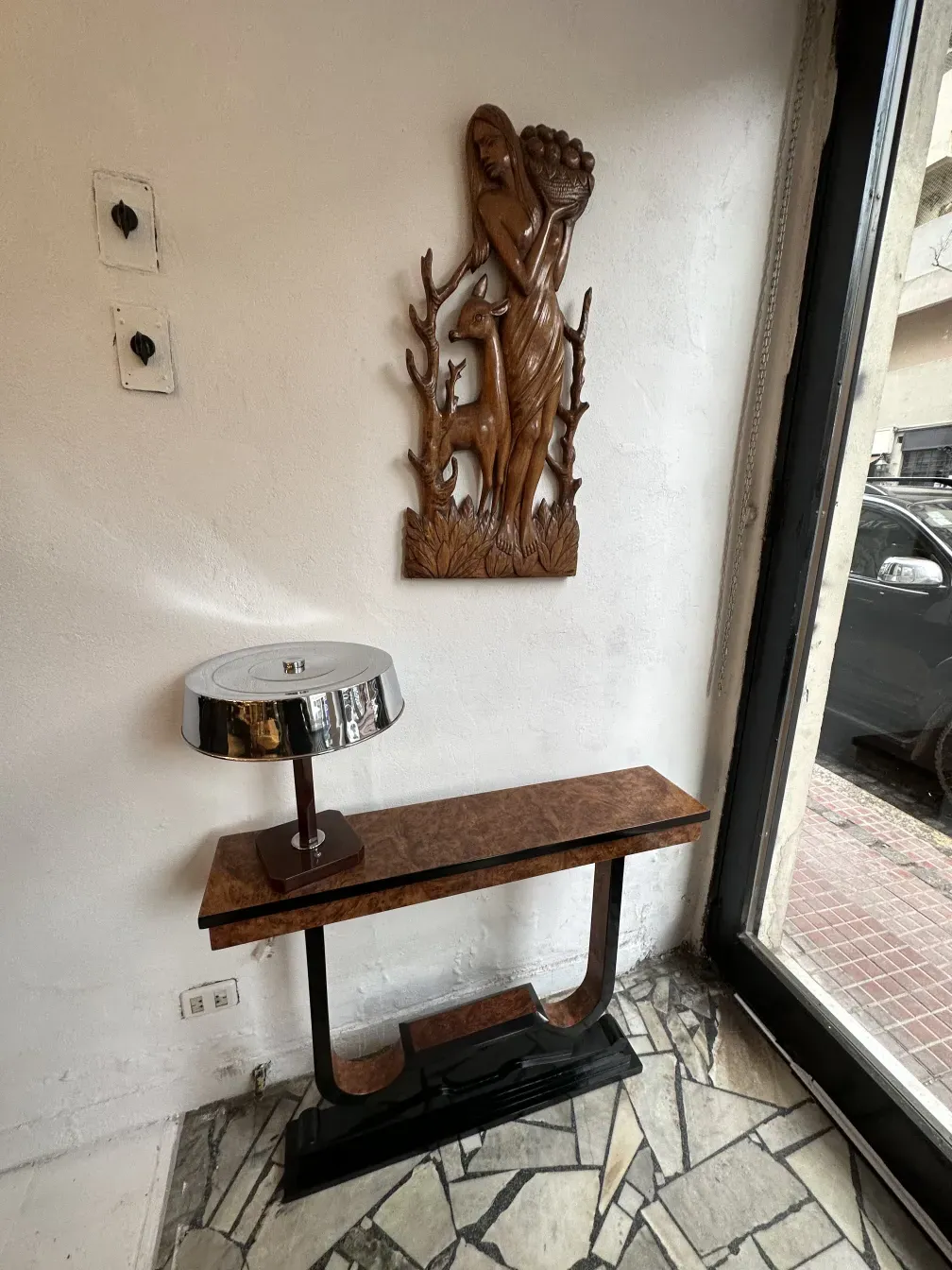 Trois consoles anciennes contre un mur blanc, à côté d'un relief décoratif.