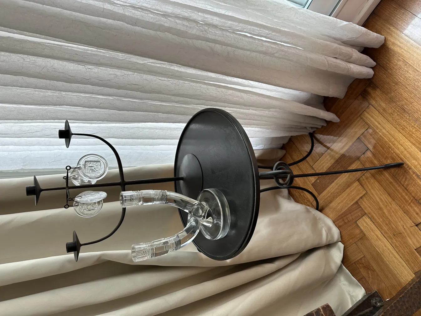 candelabro antiguo con tres soportes y un diseño elegante, situado sobre una mesa junto a cortinas blancas