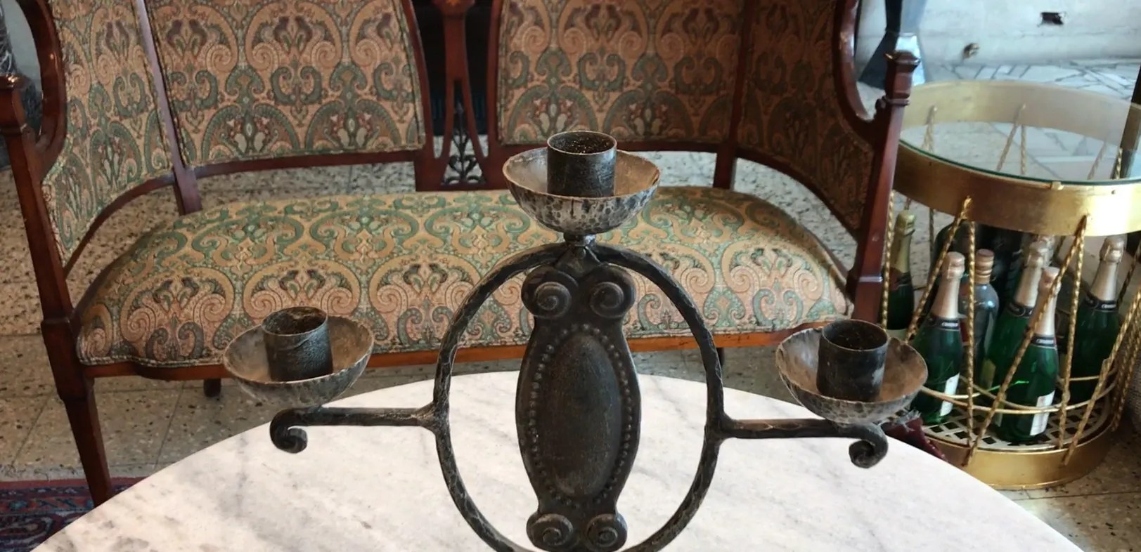 candelabro antigo com três braços e base ornamentada, fundo com móveis antigos