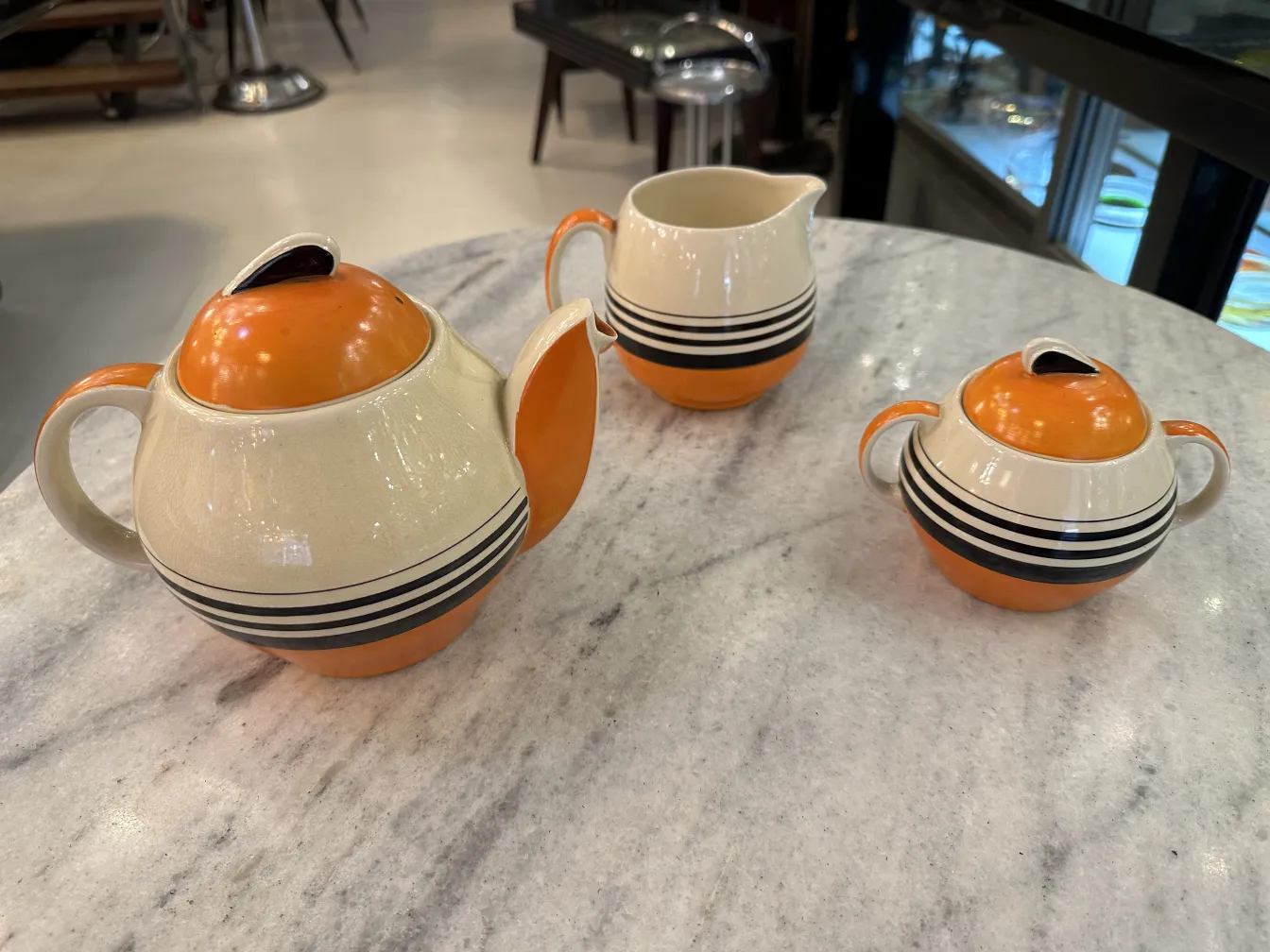 Service à thé ancien dans des tons orange et beige, avec des détails noirs. Comprend une théière et de la crème.