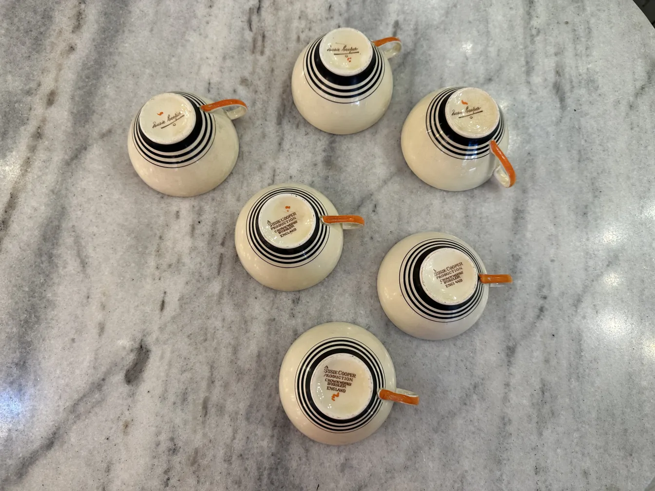 Antique tea set with six ceramic cups decorated with black and orange stripes on a marble table.