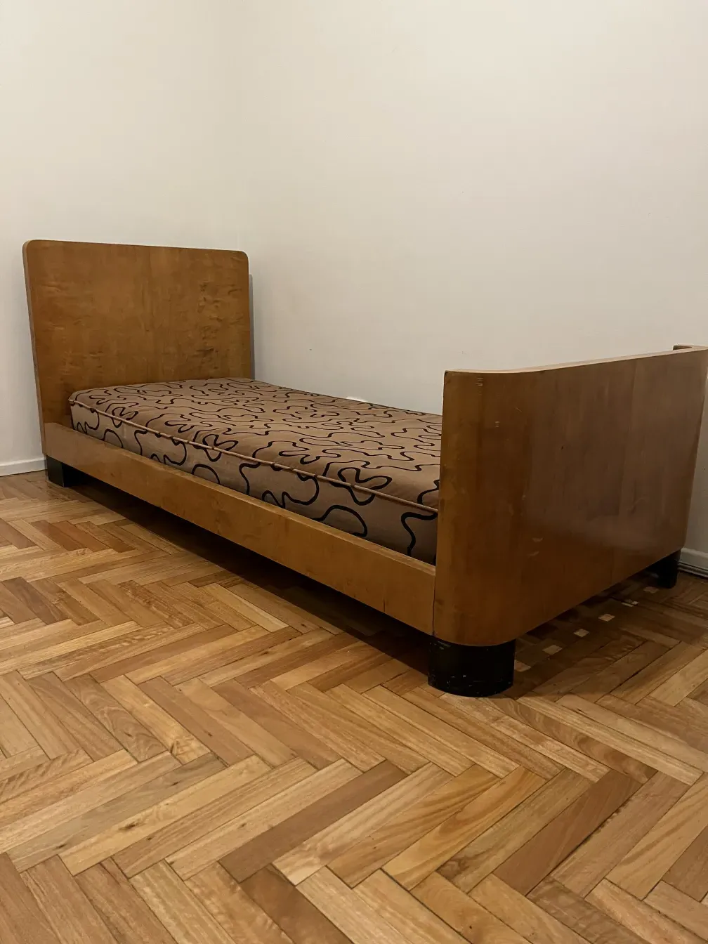 Letto antico dal design semplice con materasso decorato su pavimento in legno.