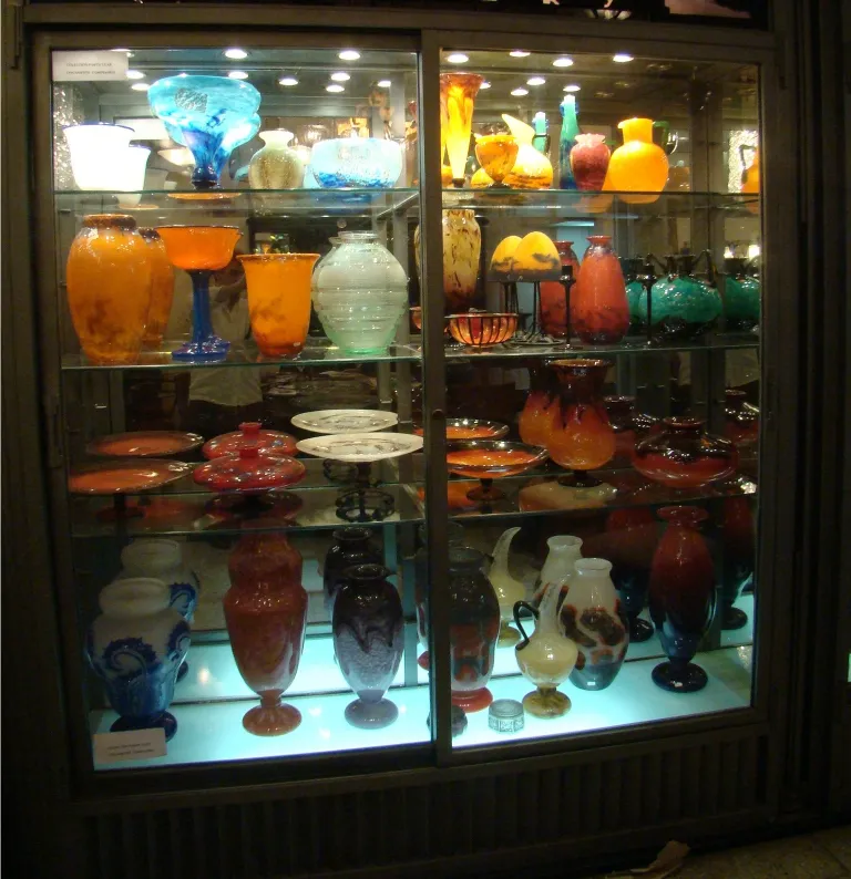 Verre antique signé Muller Freres exposé avec d'autres objets colorés.