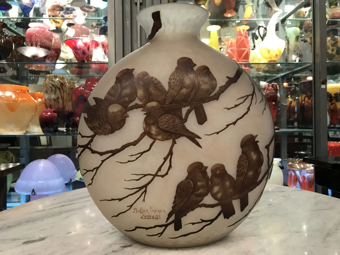 Verre ancien avec motif d'oiseaux, signé Muller Fres, en exposition avec d'autres objets.