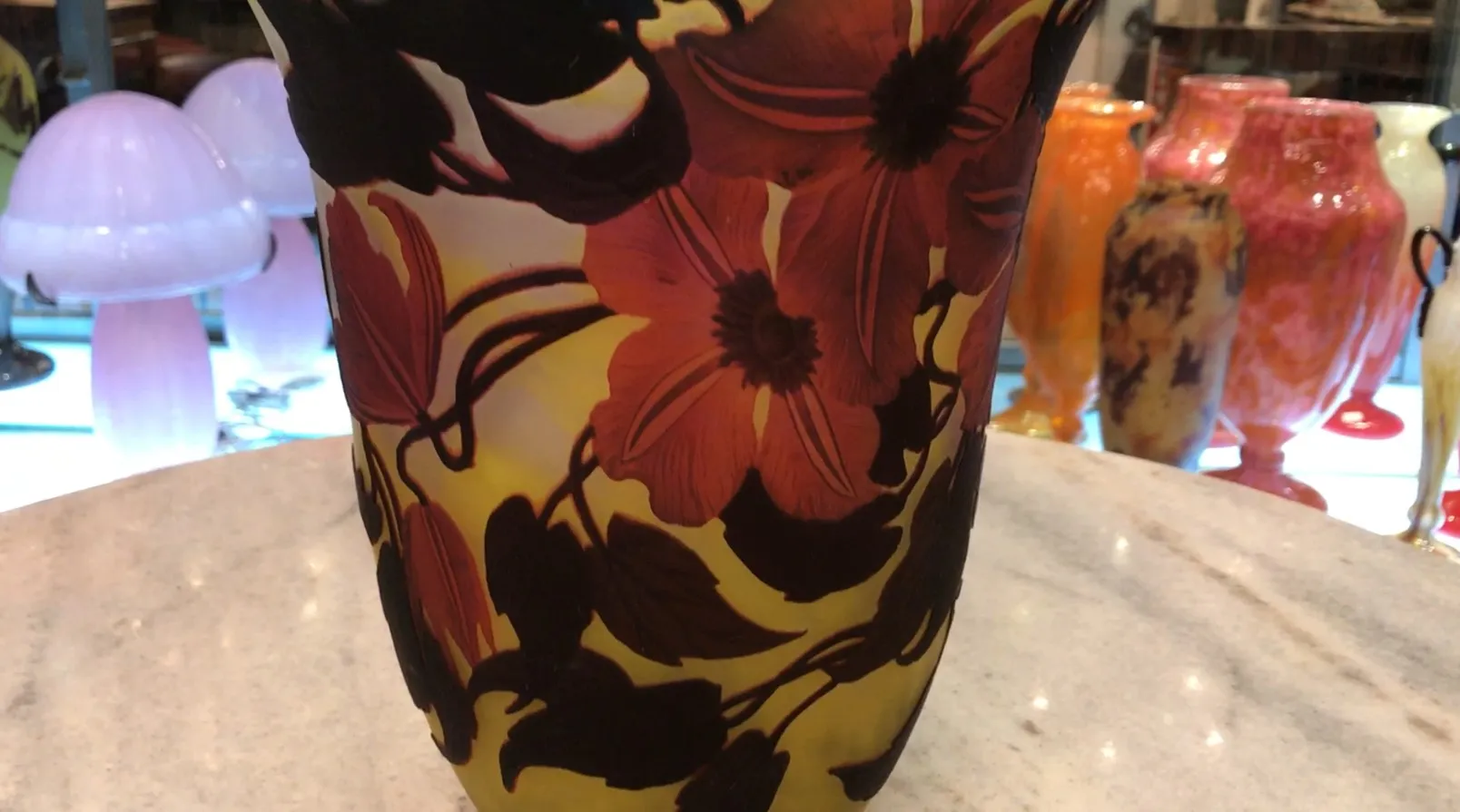 Vidro assinado Muller Freres com design floral em tons quentes, cercado por outros itens decorativos.