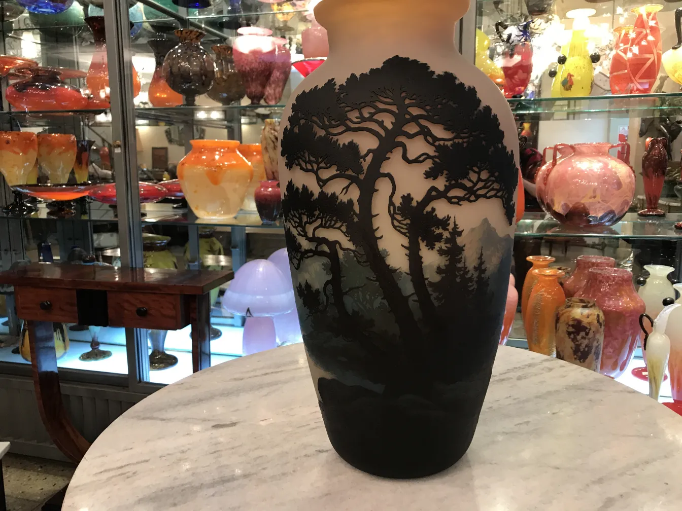 Vaso antigo de vidro assinado por Muller Fres com um design de paisagem de árvores e montanhas em um fundo colorido.