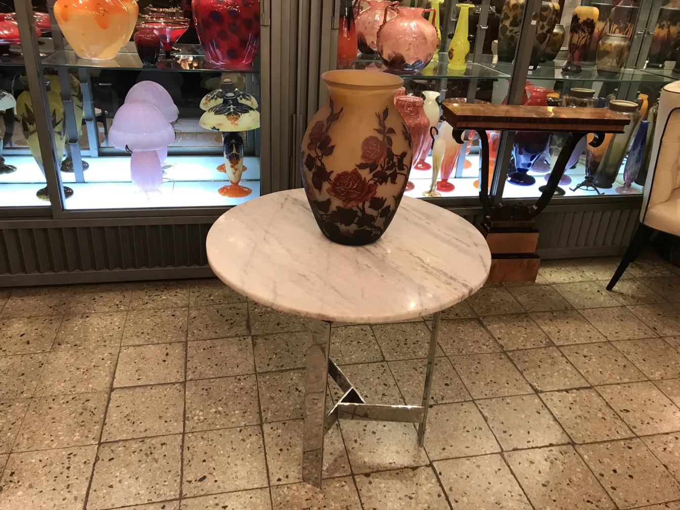 Jarrón antiguo con flores sobre mesa de mármol y vaso de vidrio firmado Muller Fres al fondo.