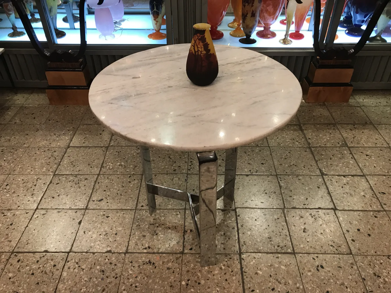 Antigua pieza de vidrio firmado muller fres en una mesa, con otros objetos decorativos en el fondo.