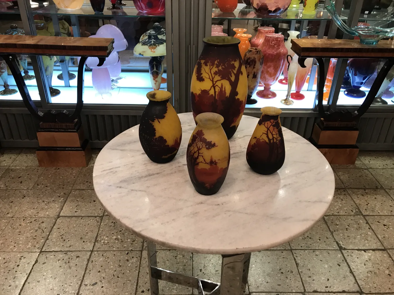 Conjunto de antiguidades, vidro assinado Muller Freres, decorado com cenas naturais, em um ambiente elegante.