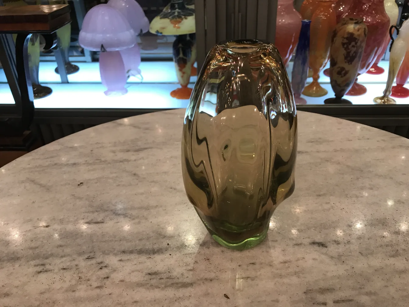 vase murano ancien de couleur claire sur une table avec des objets décoratifs en arrière-plan