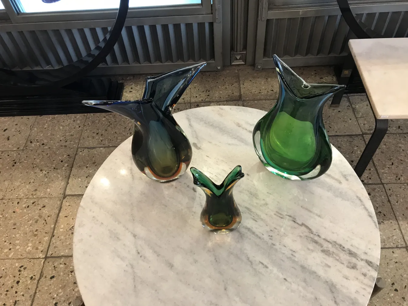 florero antiguo de murano con formas elegantes en colores verdes y negros sobre mesa de mármol